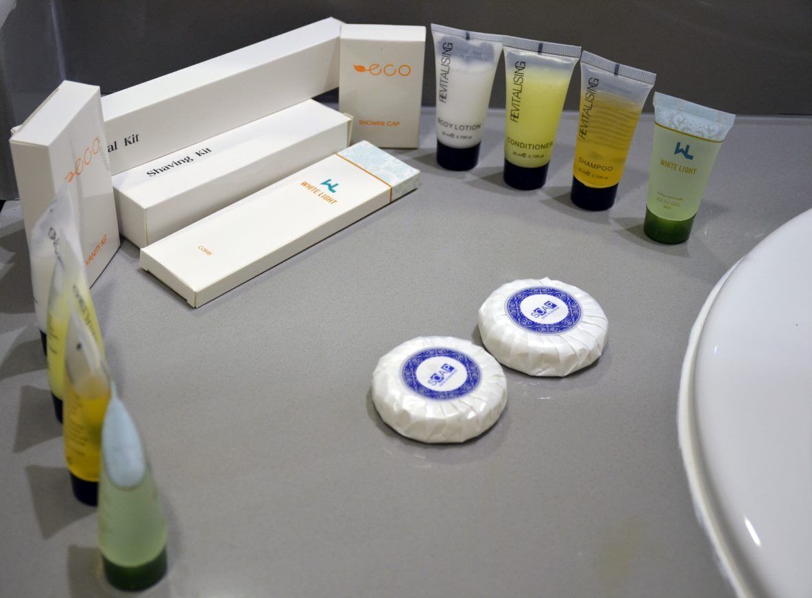 A bathroom with a shaving kit, body lotion, conditioner, shampoo, and white light products arranged on a countertop.