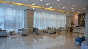 Un vestíbulo amplio con un diseño moderno, que incluye sofás, un mostrador de recepción y ventanas grandes con cortinas translúcidas.
