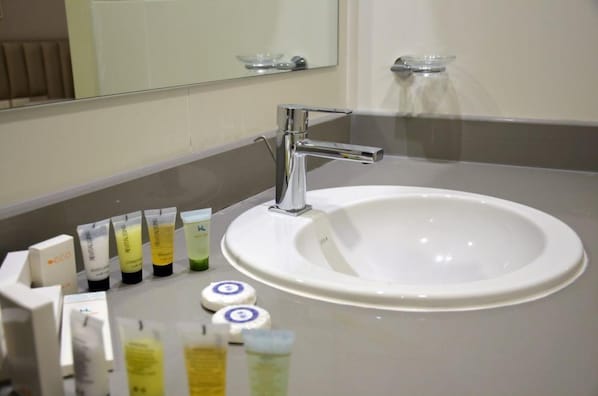 A bathroom with a white sink, chrome faucet, and a mirror above. There are toiletries on the counter. - The Lodge Suites (Manama)