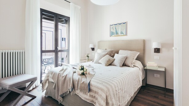 Ein Schlafzimmer mit Bett, Nachttischen, einem Fenster mit Vorhängen, einer Heizung und Blick nach draußen.
