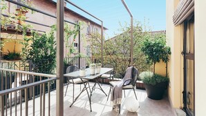 Eine Terrasses mit Tisch und Stühlen, umgeben von Kübelpflanzen und einem Metallgeländer.