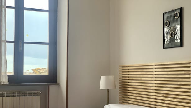 Une chambre à coucher comprenant un lit, une fenêtre, un radiateur, une table de chevet avec une lampe et une œuvre d’art accrochée au mur.