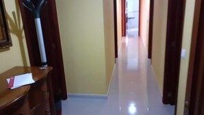 Un pasillo con un aparador de madera a la izquierda, suelo blanco y una puerta al final.