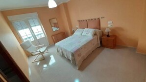 Un dormitorio con cama, mesitas de noche, una silla, una ventana y una lámpara de techo.