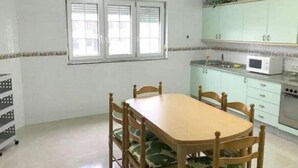 Un comedor con una mesa y sillas de madera, una ventana con persianas, un microondas y una estufa en la cocina.