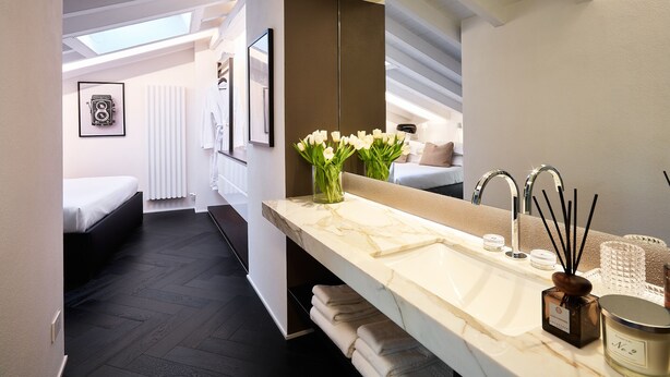 A modern bathroom with a large mirror, white sink, and a vase of white flowers.