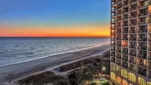 A high-rise hotel with multiple balconies overlooking a beach at sunset. - Oceanfront condo with pool & hot tub access (North Myrtle Beach)