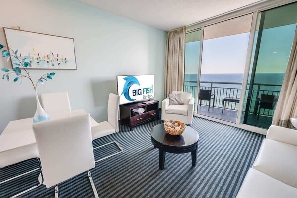 A modern hotel room with a large balcony, a flat-screen TV, and a view of the ocean.