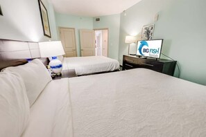 A hotel room with two beds, a TV displaying 'Big Fish Rentals', and a desk with a lamp.