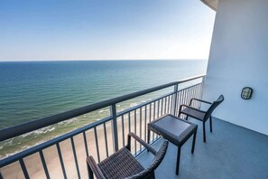Een balkon met uitzicht op de oceaan, met twee rieten stoelen en een kleine tafel.