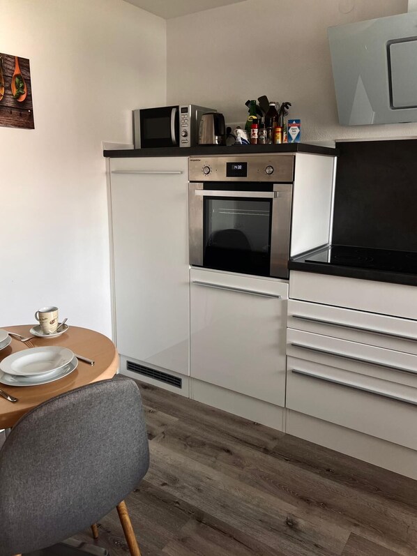 Une cuisine compacte équipée d’un four à micro-ondes, d’un four et d’une cuisinière. On y trouve une table à manger avec des assiettes et une tasse.
