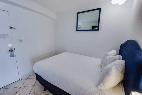 Ein Schlafzimmer mit Bett, einer Tür, einem Spiegel und einer Lampe.