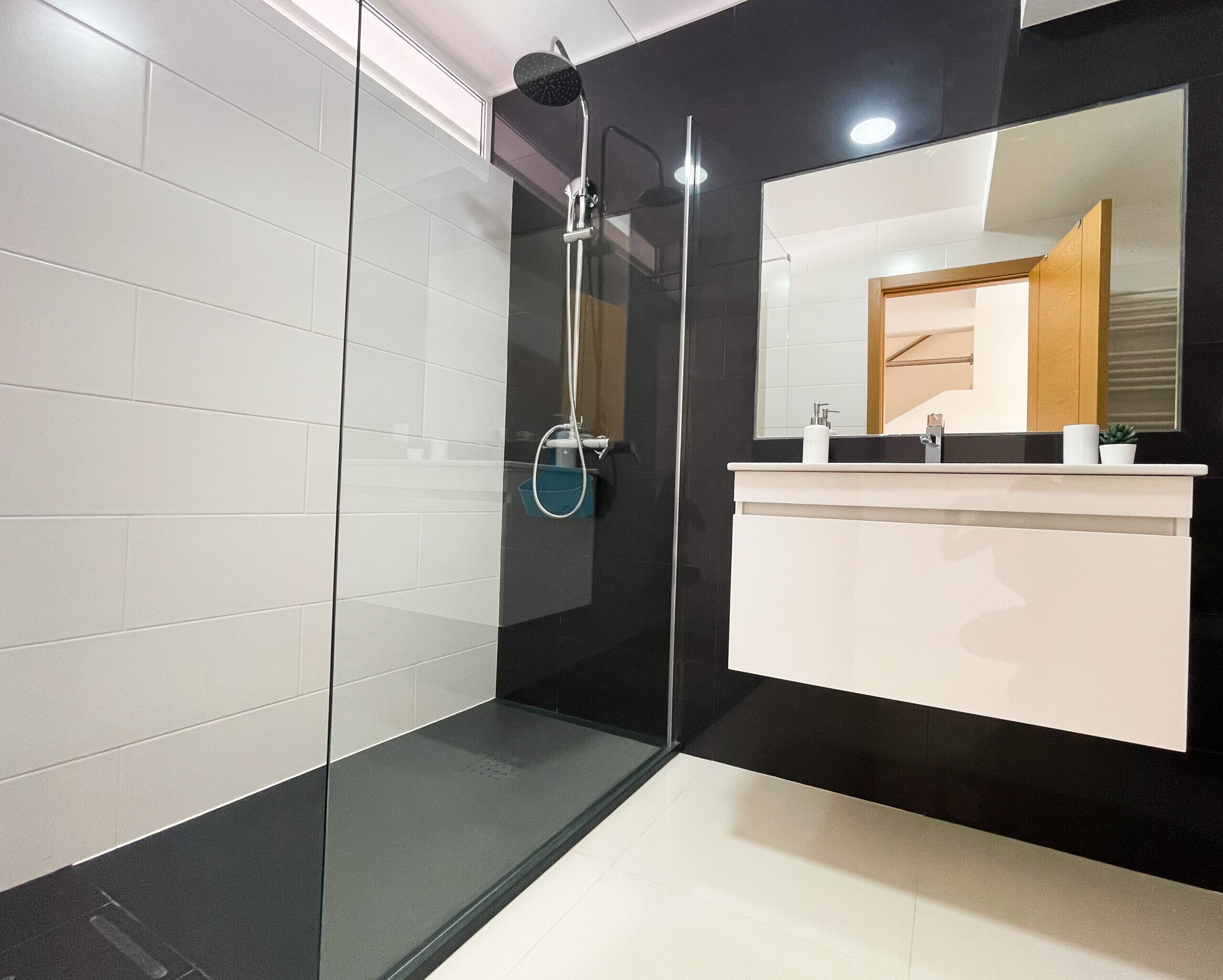 Une salle de bain moderne avec une douche à parois de verre, un lavabo blanc et un grand miroir.