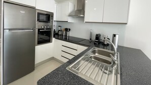 A modern kitchen with white cabinets, a stainless steel refrigerator, an oven, a microwave, a sink, and a coffee maker. - Casa Rosa - Vilamoura (Vilamoura)