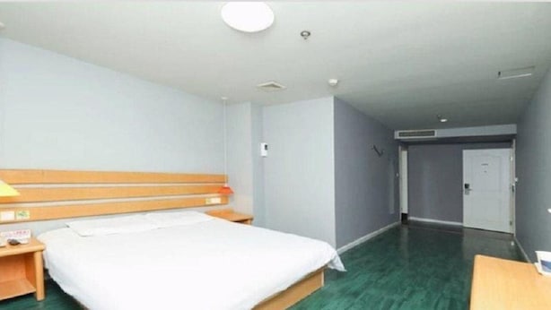 Hotellihuone, jossa on sänky, puinen pääty, yöpöydät ja vihreä lattia.