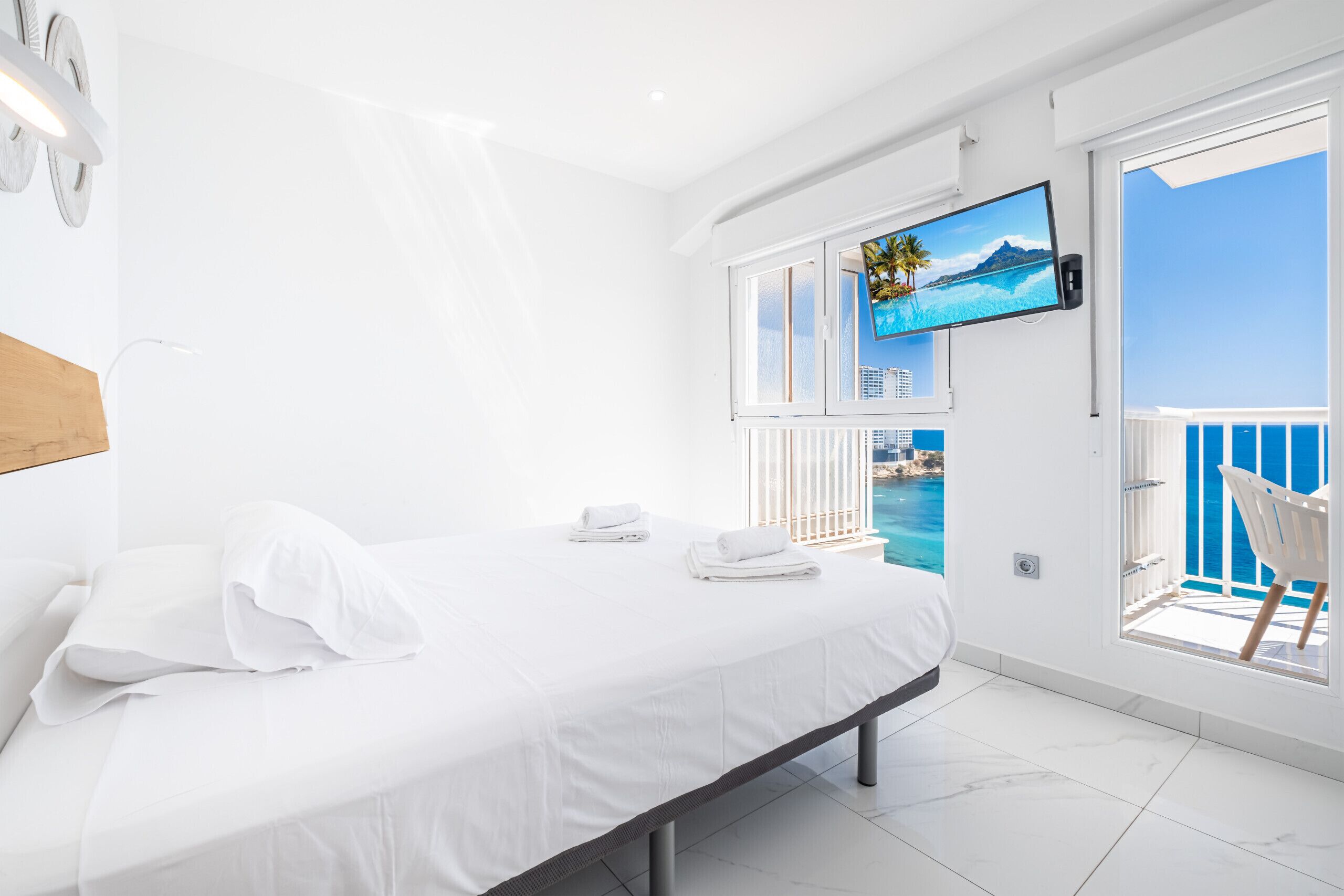 Ett modernt hotellrum med en säng, en tv som är monterad på väggen och en balkong med utsikt över havet.
