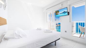 Ett modernt hotellrum med en säng, en tv som är monterad på väggen och en balkong med utsikt över havet.