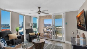 Un salón amplio con un gran ventanal, ventilador de techo, balcón con vistas a la ciudad y zona de comedor.