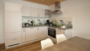 A modern kitchen with white cabinets, a built-in oven, and a dining area with a table and chairs. - Ferienwohnung Wiesenblume UR (Beilngries)