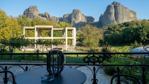 Un patio con mesa y sillas, barandilla de metal, y vistas a formaciones rocosas y vegetación.
