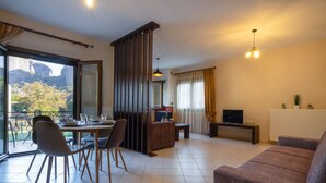 Una sala de estar moderna con comedor, un sofá, un televisor y un balcón con vista a montañas.
