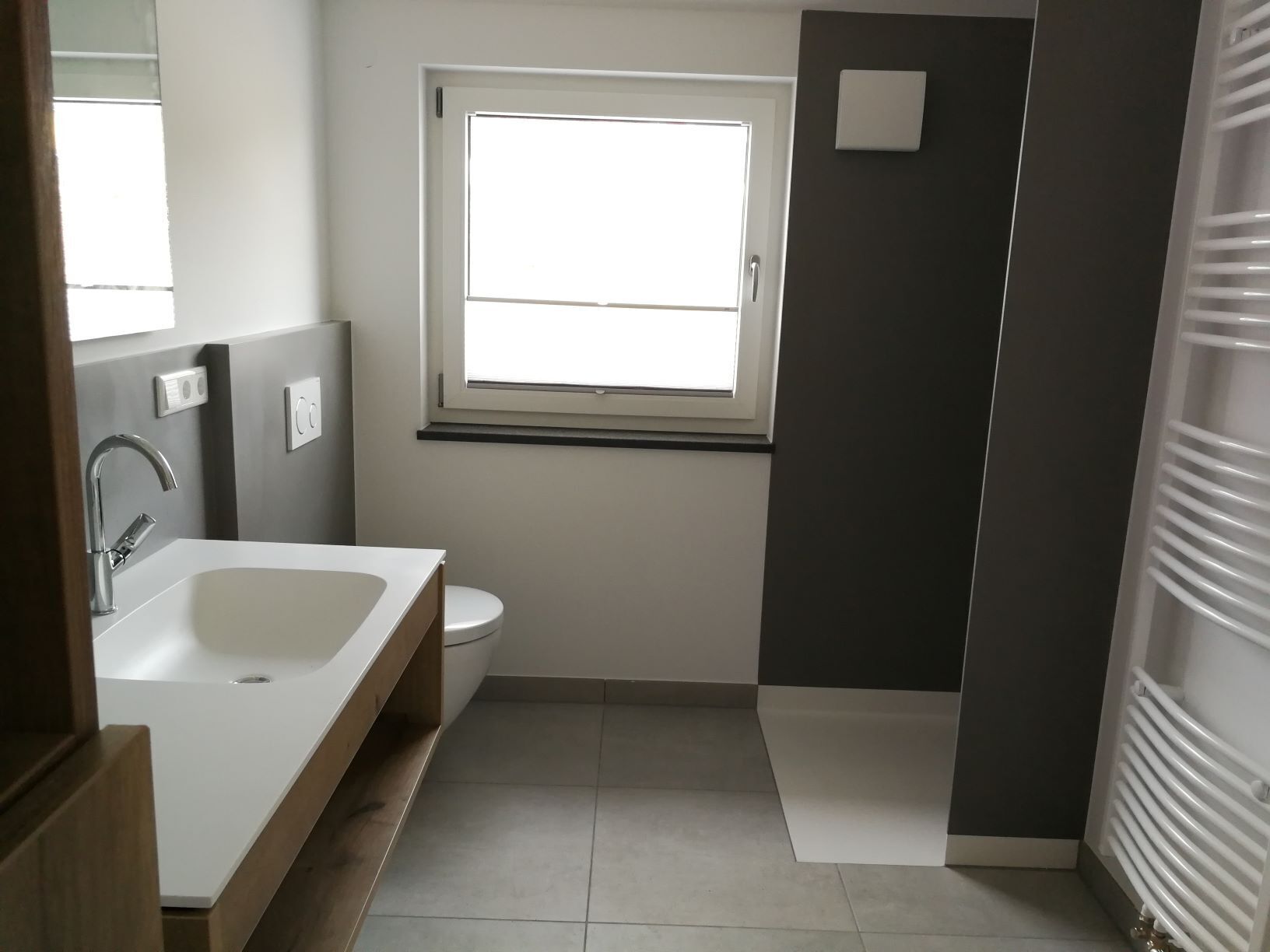 Un baño moderno con un lavamanos blanco, un inodoro y una ventana.