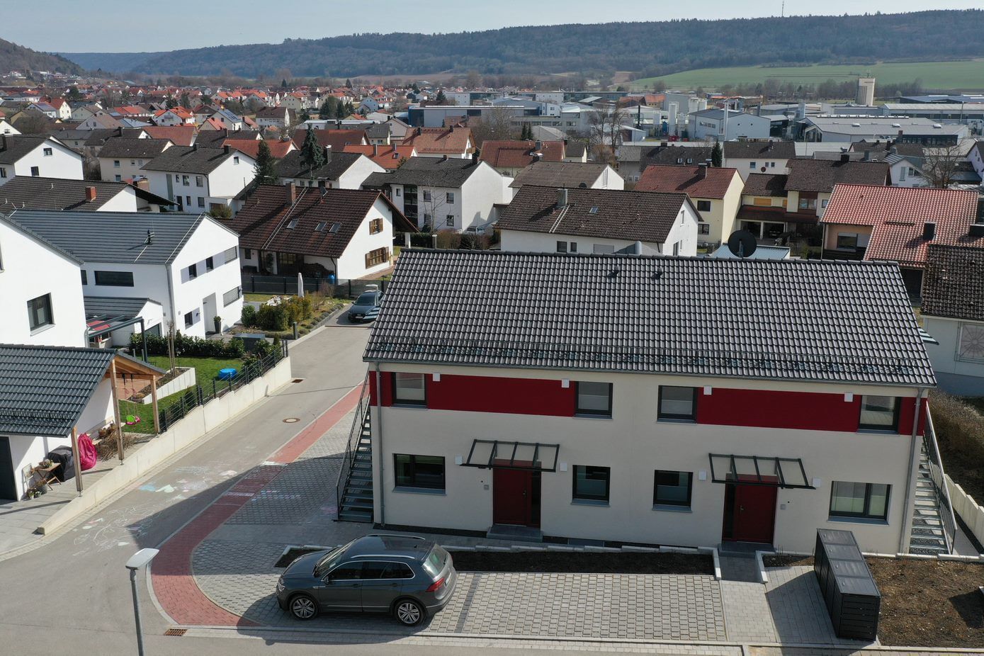 A residential area with a two-story building featuring a red and white facade, a paved driveway, and a parked car.