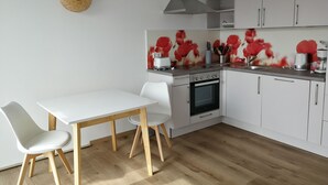 A modern kitchen with white cabinetry, a wooden dining table with chairs, a stove, and a microwave. - Ferienwohnung Ranunkel (Beilngries)
