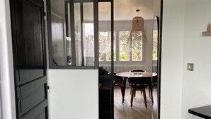 A modern kitchen with a black refrigerator, a dining area with a wooden table and chairs, and a view of the outdoors through large windows.