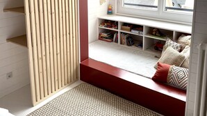 A cozy room with a built-in window seat, wooden shelves, and a woven rug.