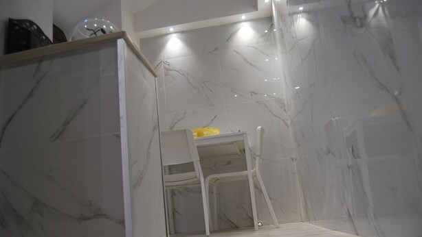 A bathroom with a marble floor and walls, a white chair, and a shower area.