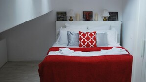 A neatly made bed with a red and white bedspread, white pillows, and a red patterned pillow.