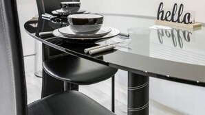 Een moderne eetruimte met een zwart-wit kleurenschema, met een ronde tafel met glazen blad, zwarte stoelen en een bord waarop 'hello' staat.