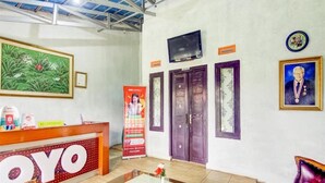 A hotel reception area with a reception desk, a large framed painting, a television mounted on the wall, and a framed portrait. - Spot ON 90046 Villa Anyelir Yustik Selabintana (Sukabumi)