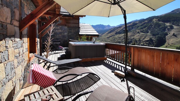 Una terraza de madera con mobiliario exterior, un jacuzzi y vistas a las montañas.