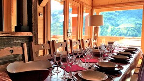 Una mesa de madera dispuesta para una comida, con sillas, copas de vino y platos.