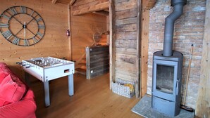 Una habitación acogedora con interior de madera, una mesa de fútbol, un reloj de pared grande y un estufa de leña.