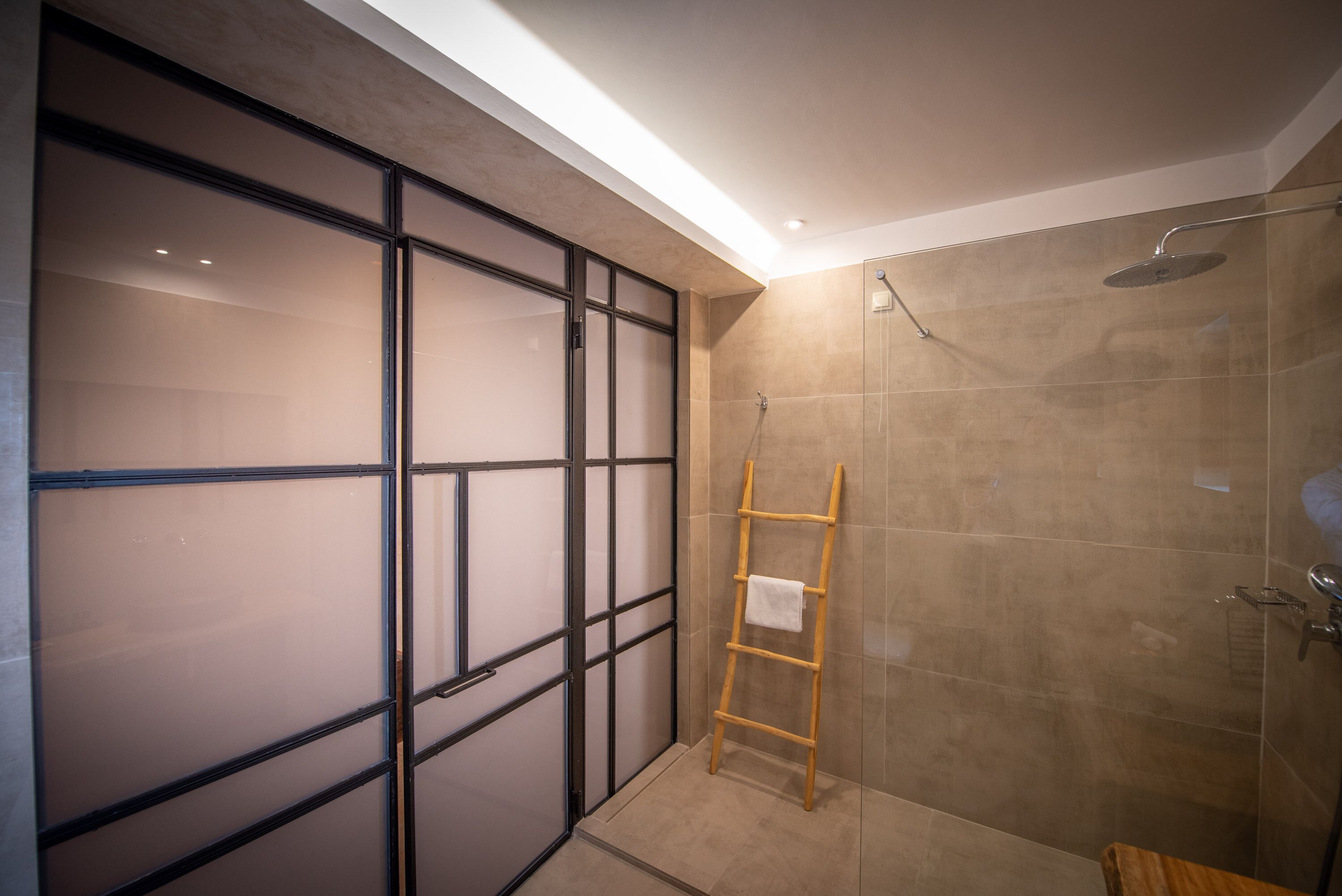 A modern bathroom with a glass shower enclosure, a wooden ladder, and a sliding door.