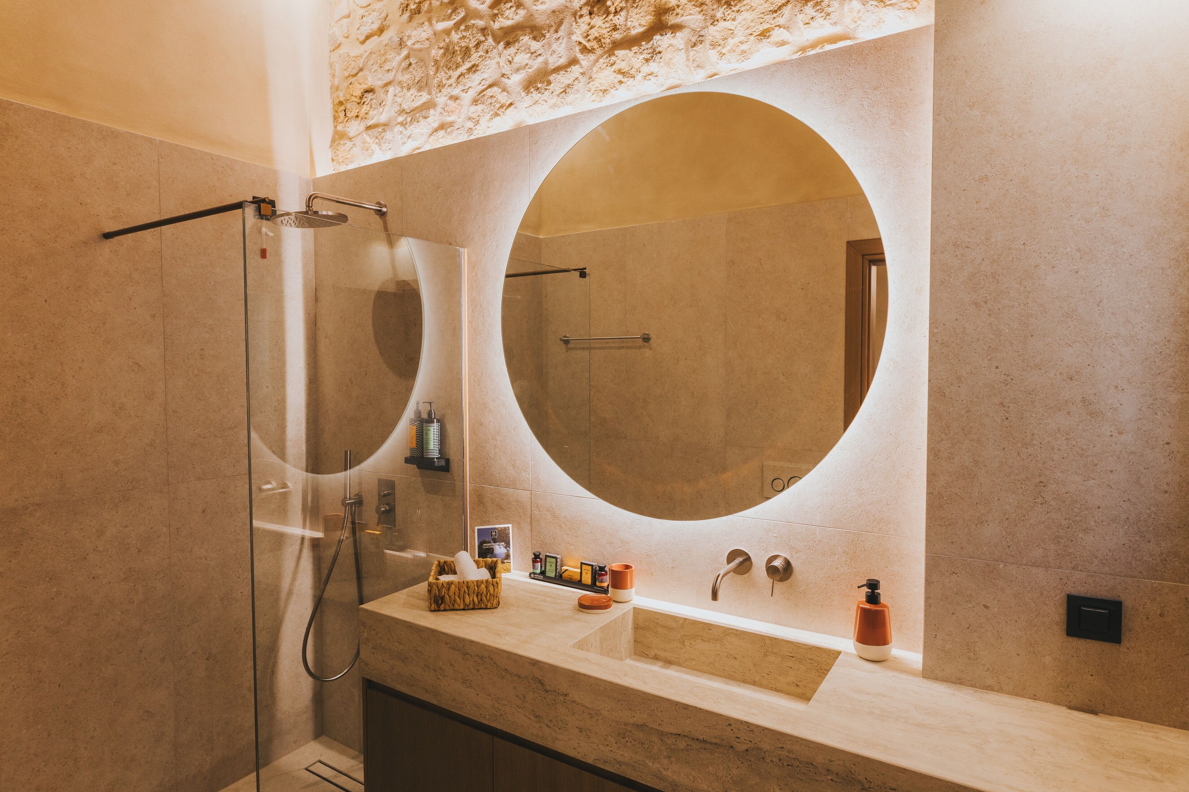A modern bathroom with a large oval mirror, a glass-enclosed shower, and a marble countertop.