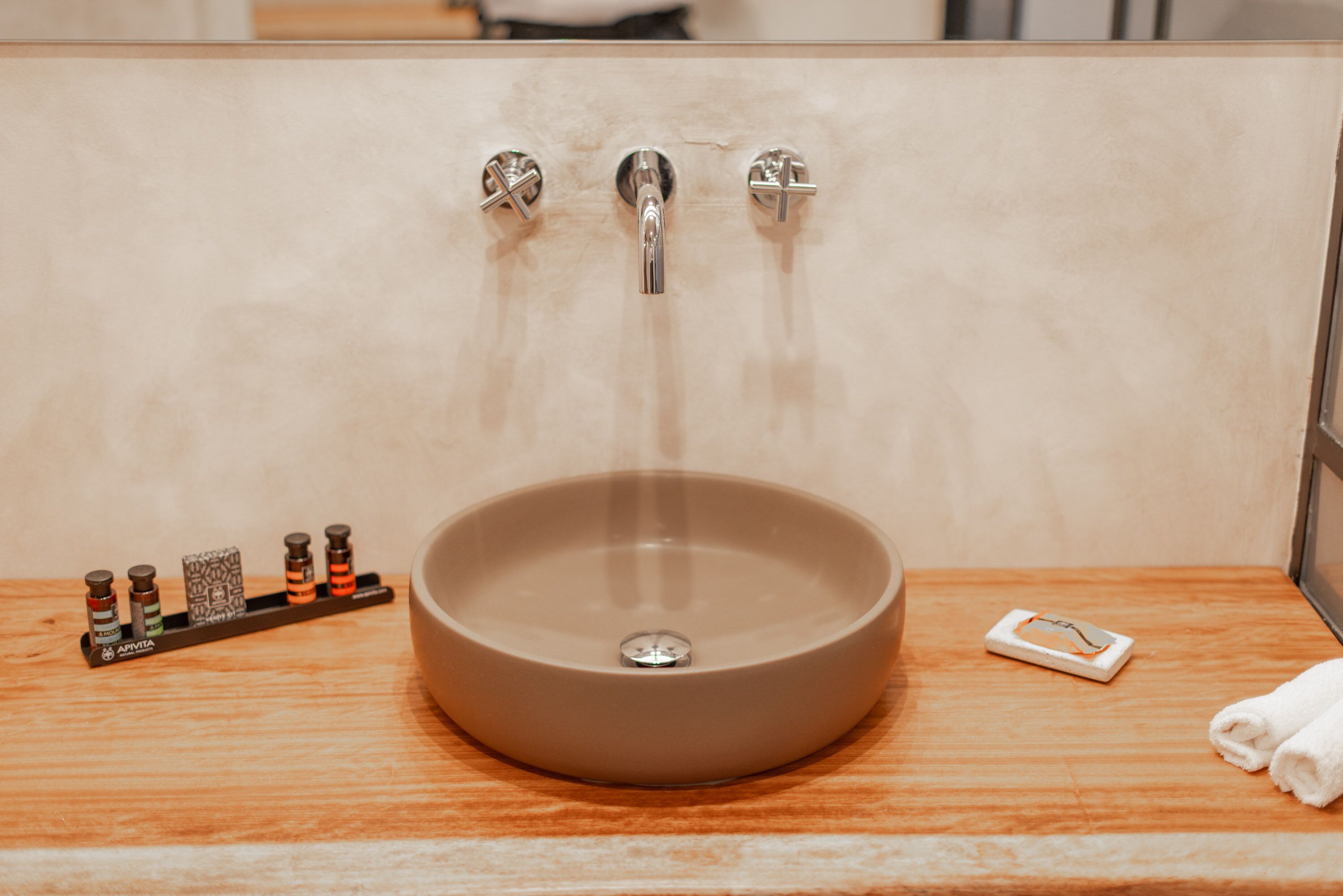 Un baño con un lavabo redondo, dos grifos y un jabonera con botellas.