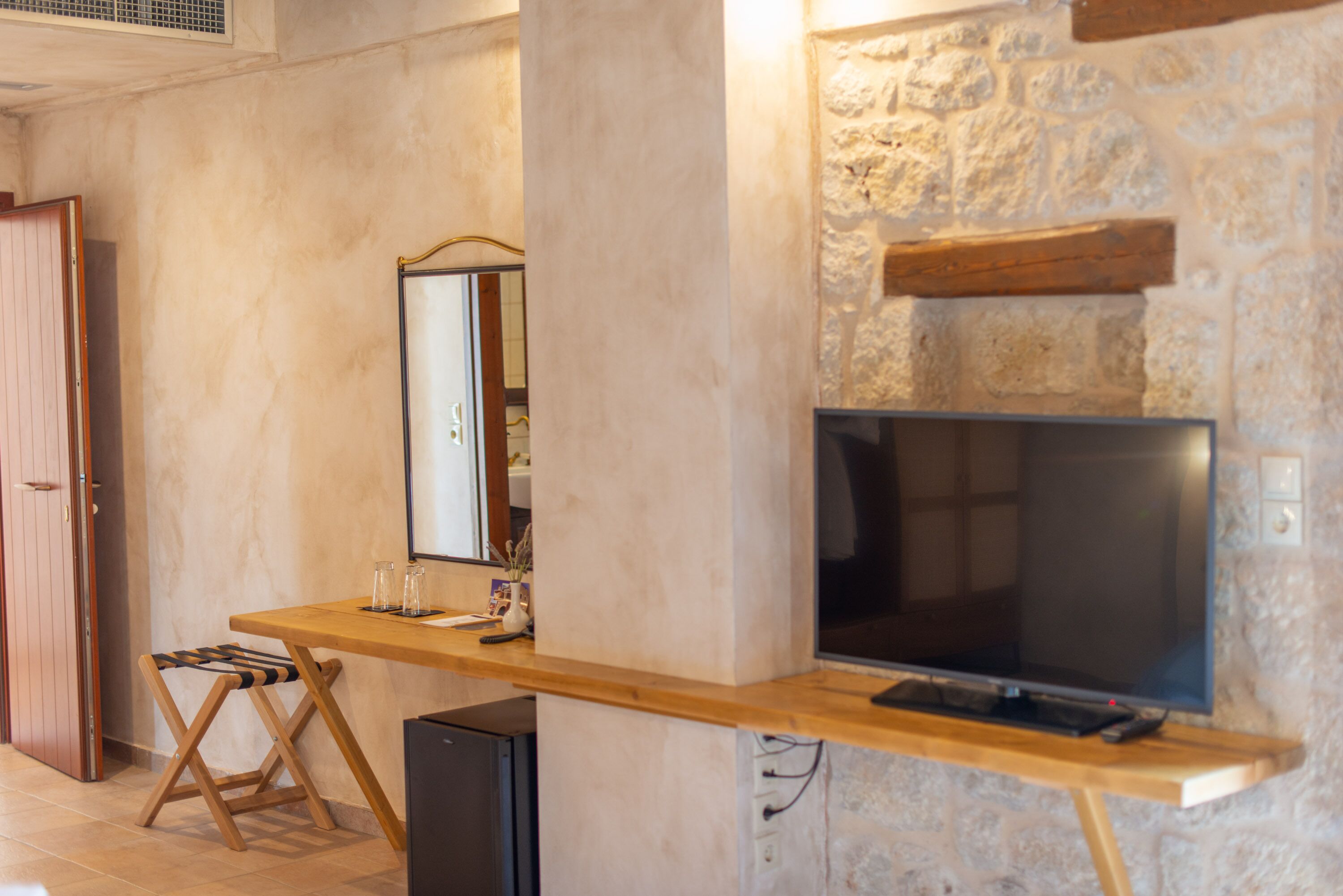 A room with a wooden desk, a television, a mirror, and a stone wall.