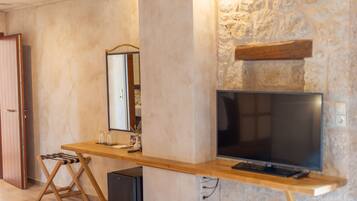 A room with a wooden desk, a television, a mirror, and a stone wall.