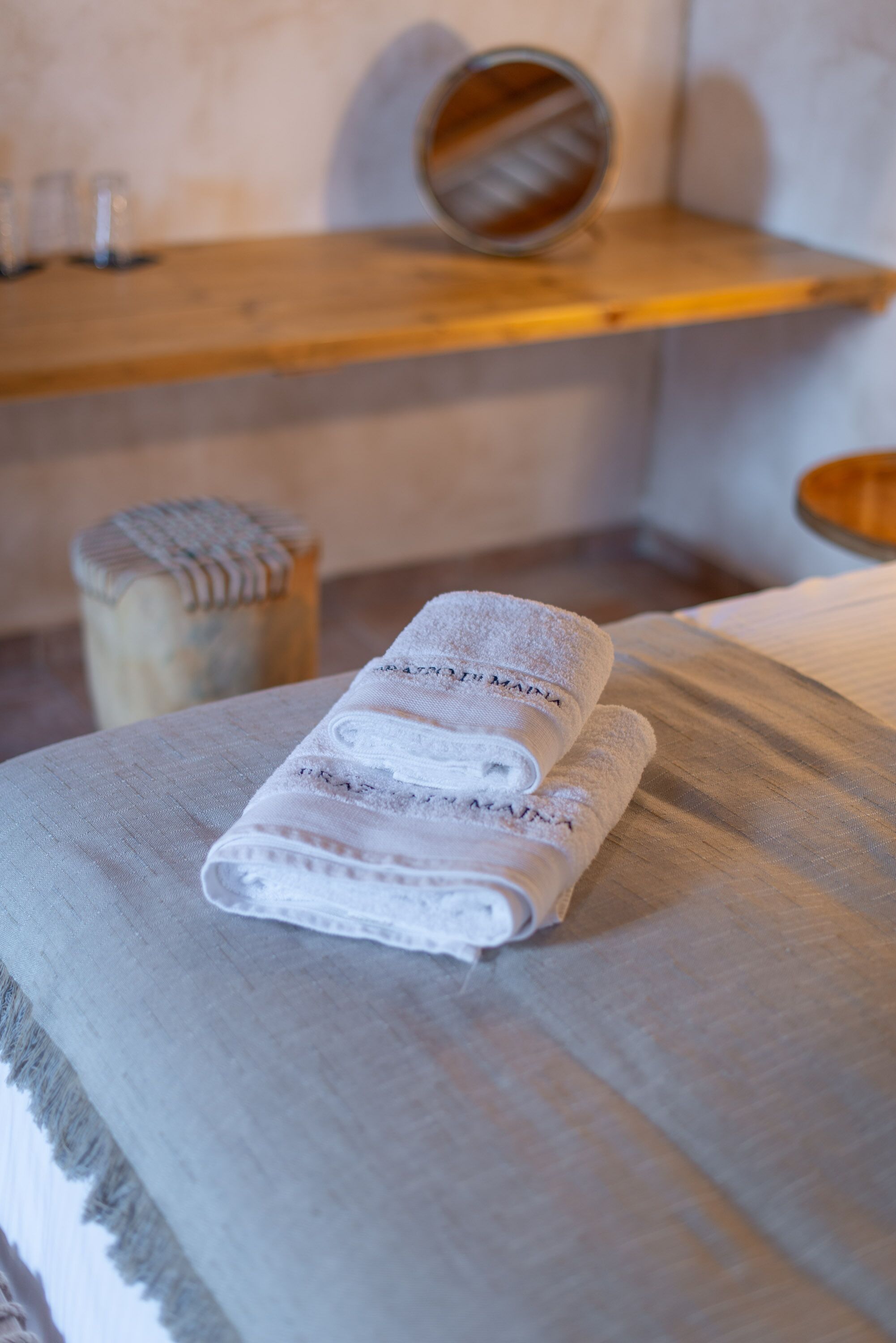 A neatly made bed with folded towels and a wooden bench with a mirror.
