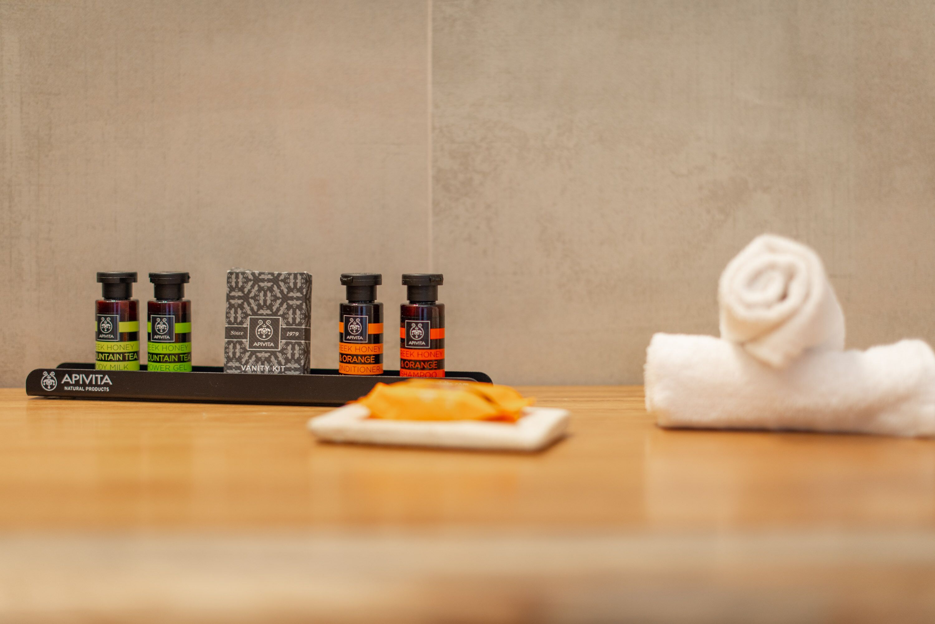 Una mesa de madera con cuatro botellas de productos Apivita, una toalla blanca y una servilleta doblada.