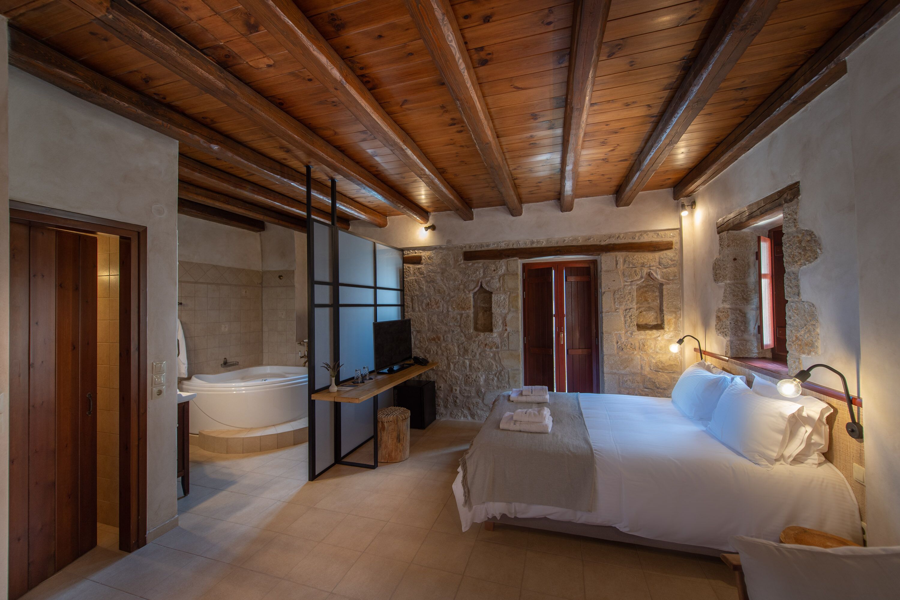 Ein Schlafzimmer mit Holzboden, Steinwänden, einem großen Bett, einem Fernseher und einer Badewanne.