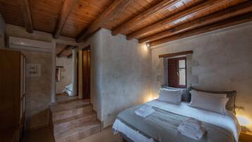 Un dormitorio con techo de madera, una cama con ropa blanca, una escalera y un ventanal pequeño.