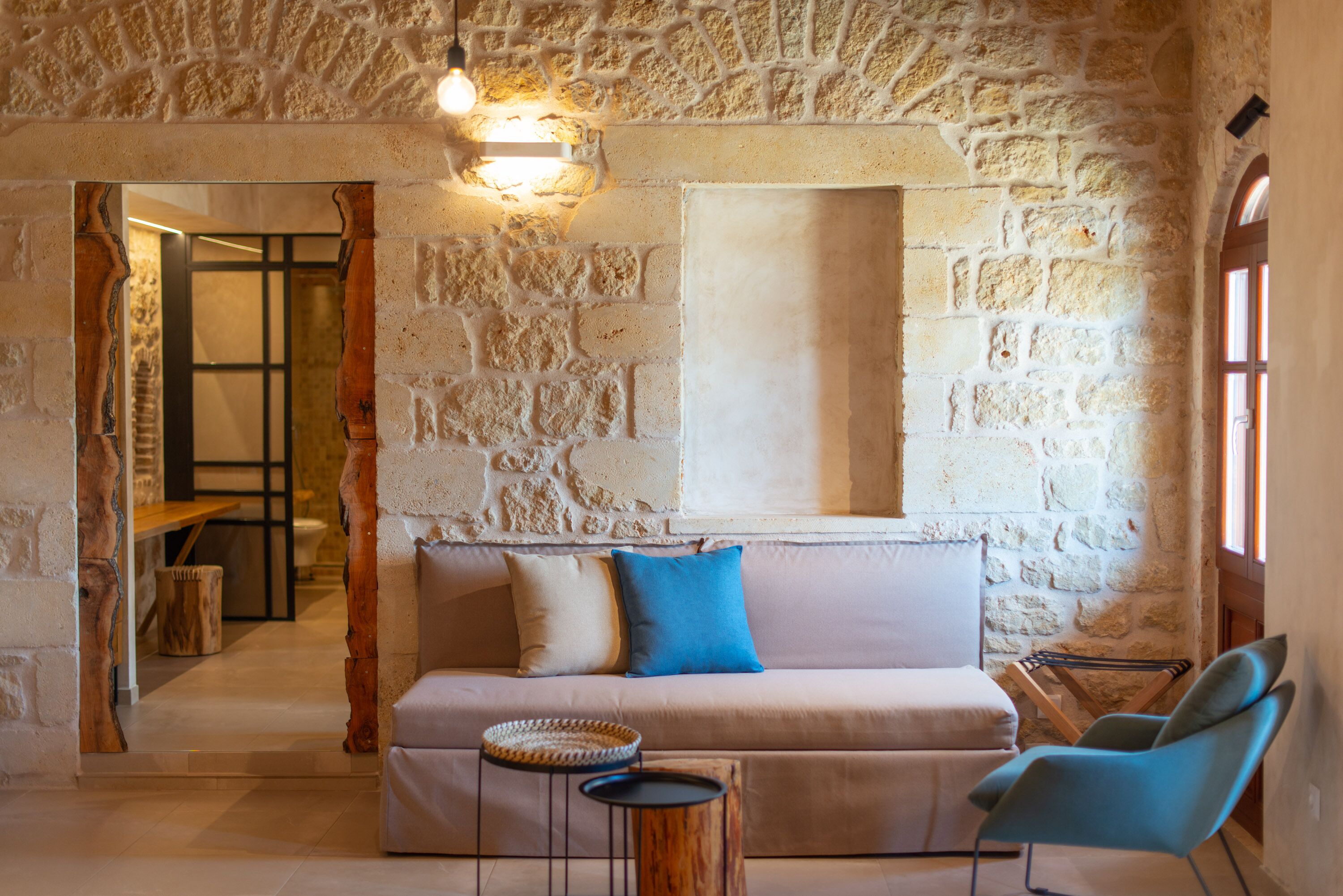 A cozy room with a stone wall, a sofa with cushions, a small wooden table, and a blue chair.
