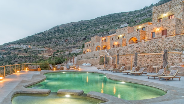 A pool area with lounge chairs and a stone building in the background. - Brazzo di Maina (East Mani)