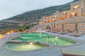 Un área de piscina con sillas de descanso y un edificio de piedra al fondo.