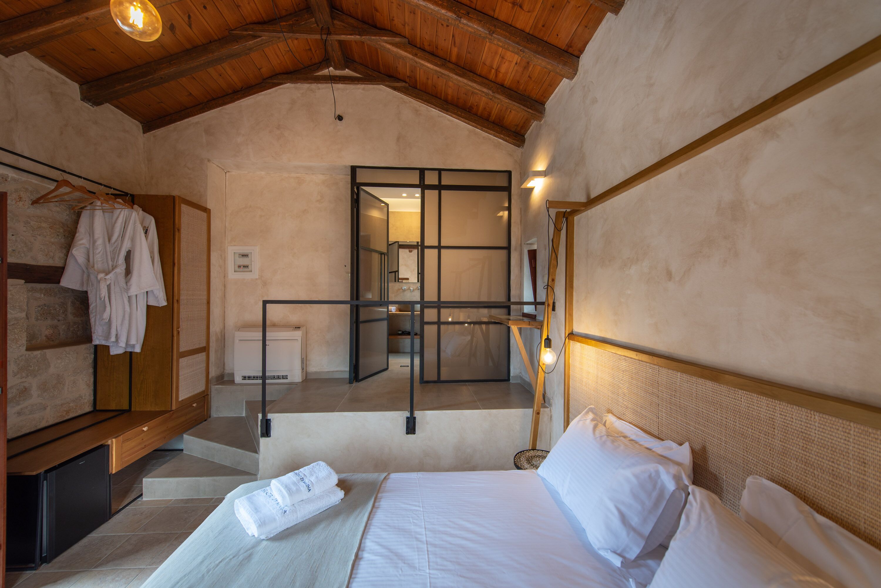 A bedroom with a wooden ceiling, a bed with white linens, a wooden bench, and a towel on the bed.